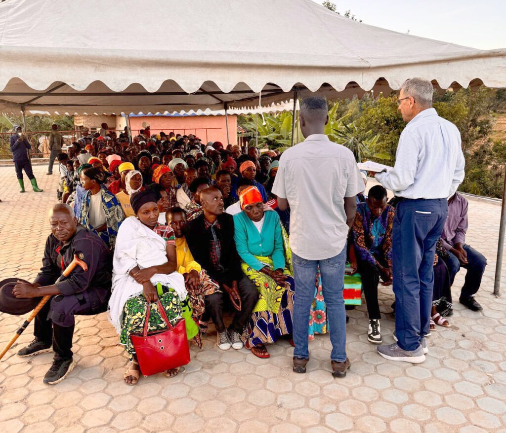 Bob preaches in front of a group of people seated in chairs in front of the medical center.
